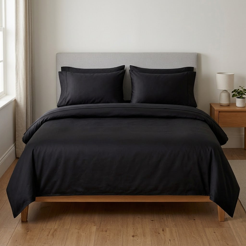 Black brushed microfibre sheet set on a made bed, showing the fitted sheet, turned-back flat sheet and two pillowcases